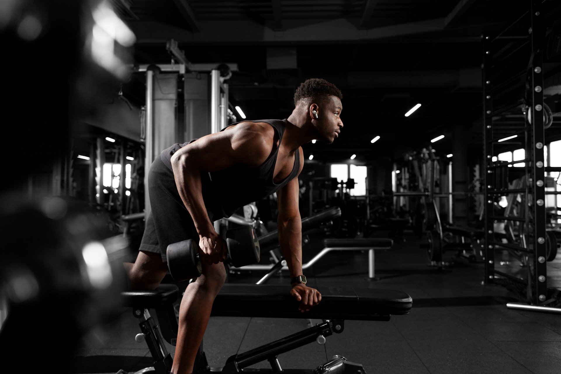 athletic african american man trains in dark gym, athletic guy lifts heavy dumbbells in fitness club